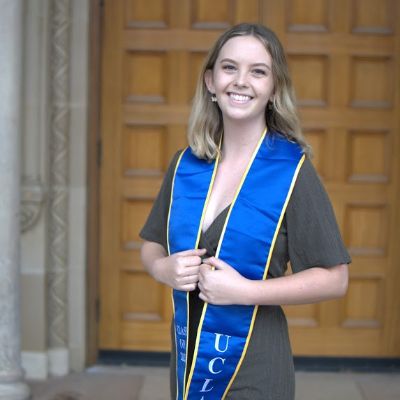 photo of Julianne posing in front of building with a graduation stole and smiling at the camera